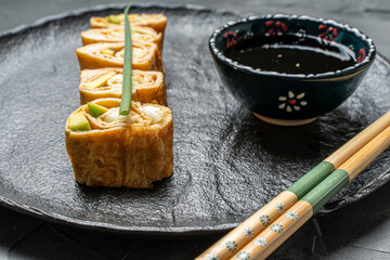 Tamagoyaki or a traditional Japanese omelet roll with avacado and cheese on a black mica plate with soy sauce and chopsticks. High quality photo