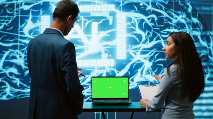 Startup coworkers looking over charts, using AI software on mockup laptop to take data driven...