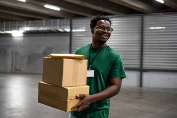 Smiling black delivery man sorting parcels inside warehouse.
