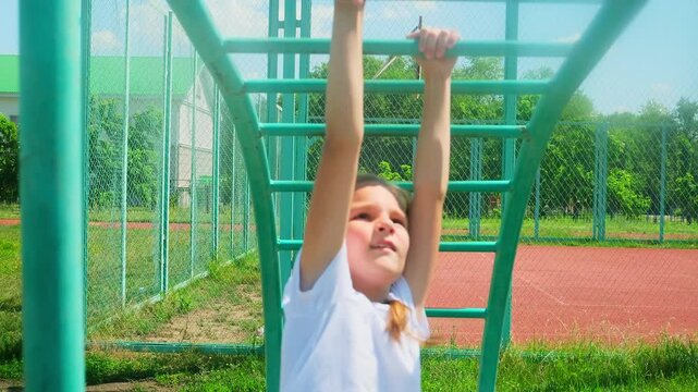 Strong cute 8 year old girl exercising on monkey bars outdoor on sport ground. Slow motion, 4K