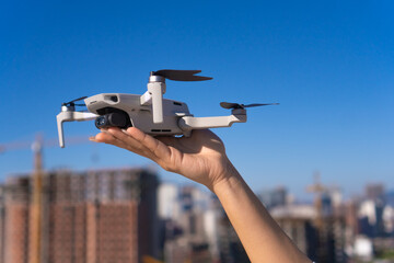 Close-up of a woman's hand holding a drone in the palm of her hand on a sunny day. Surveyor engineer plans to inspect the construction site using a drone.