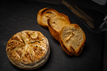 Camembert or brie cheese baked in the oven on a black background with toasted bread or toast. Copyspace. High quality photo