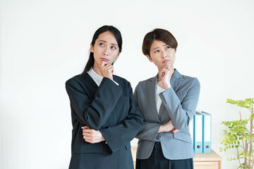 白背景でネガティブに考えるスーツを着た女性二人