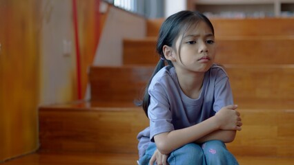 An Asian girl sits on the stairs with a bored expression on her face. Her dim eyes reflect her disinterest in her surroundings.