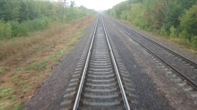 Video footage from the last carriage of the train. Rails running away into the distance. A summer or autumn cloudy day.