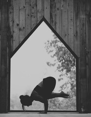 Woman doing Vinyasa yoga handstand pose close to a window with black fitness outfit wooden room natural light black and white