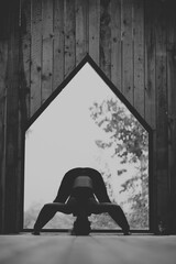 Woman doing Vinyasa yoga pose close to a window with black fitness outfit wooden room natural light black and white