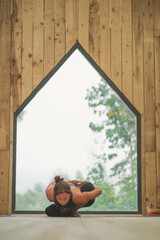 Woman doing Vinyasa yoga pose close to a window with black fitness outfit wooden room natural light