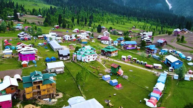 Aerial view of Arang Kel village in Kashmir, surrounded by lush green forests and scenic landscapes, showcasing traditional wooden architecture.push forward