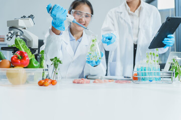 Two Asian women in a lab work on food research, using a microscope, petri dish, and test tubes...