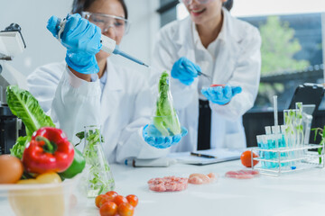 Two Asian women in a lab work on food research, using a microscope, petri dish, and test tubes...