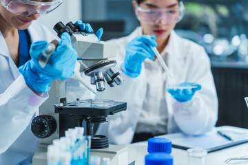Two Asian women in a lab work on food research, using a microscope, petri dish, and test tubes...