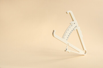 Plastic body fat caliper on beige background. Space for text