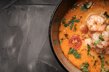 Tom Yam Kung Spicy Thai soup with shrimp and cilantro in a bowl on a dark background of a black mica board. Top view, close-up. Copyspace.