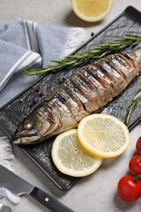 Delicious grilled mackerel, rosemary, lemon and tomatoes on grey table, closeup