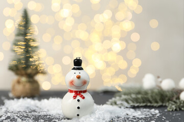 Funny snowman figure and artificial snow on table against blurred lights