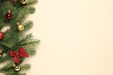 Fir tree branches with Christmas balls and bow on beige background, flat lay. Space for text