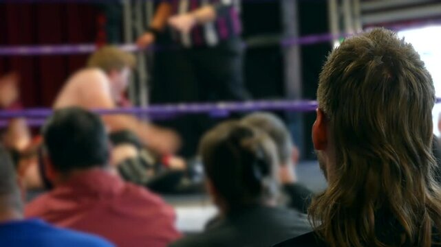 A group of spectators watching an intense wrestling match, with the action unfolding in the ring as one wrestler pins another.