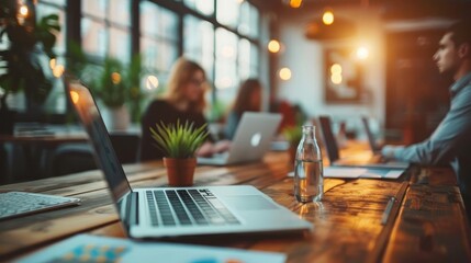 Modern open office space with laptops, bottle, and plants, showcasing a collaborative working environment with natural lighting.