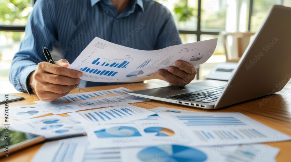 Leinwandbilder a business executive analyzing a printed report with various graphs and charts, seated at a desk wit