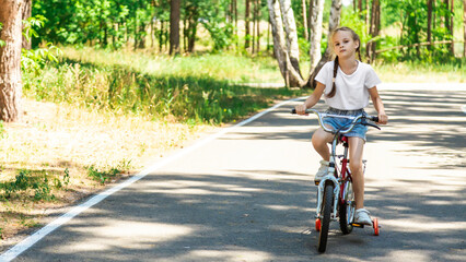 Fototapeta premium Child riding a bike in summer park. Children learning to drive a bicycle on a driveway outside. Kid riding bike. Child on bicycle, bike outdoor.