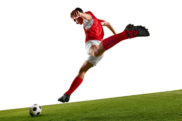 Football player in red-white, executing powerful kick while training on green field, in motion against white studio backdrop. Concept of championship, sport events, final game. Ad
