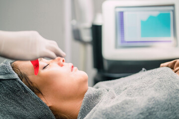 surgery person putting eye mask woman for therapy. female patient relax while cosmetologist applying collagen patch under eye. surgeon using red pad stick under patient eye for beautiful operation