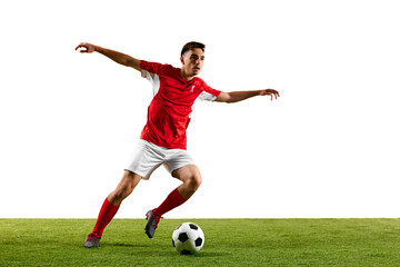 Football player dressed in red-white uniform, preparing for long-range pass, locked in action as he swings his leg mid-air during practice on green pitch. Concept of sport events, final game. Ad