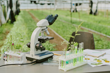 Microscope on laboratory table surrounded by plants and test tubes in modern greenhouse environment...