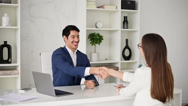 A professional handshake between a man and a woman , seated across from each other in a stylish office. The handshake signifies the sealing of a successful deal or conclusion of positive job interview