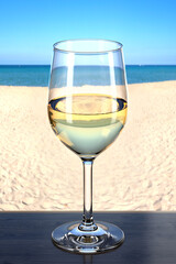 Glass of white wine on the wooden table in the beach bar. Picturesque background with sand and sea. Glassware with the drink. 3d rendering.