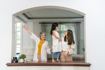 Obraz premium Three generation asian family together at home, happy grandmother, mother and daughter bonding, standing by window arch, family love and connection, lifestyle of asian family with different ages