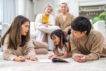 Asian father and mother with daughter bonding time, learning and reading book together on floor, family education at home, nurturing childhood development, happy love asian family indoors, lifestyle