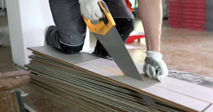 Carpenter with saw cuts laminate sheet and installs floor in home renovation. Installation laying flooring