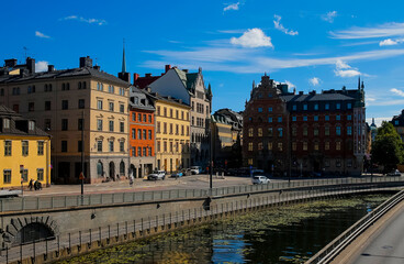 Naklejka premium Colorful historic buildings along a riverbank in Stockholm on a bright sunny day. Historic buildings in vibrant colors line a riverbank in Stockholm, showcasing the city's architecture.