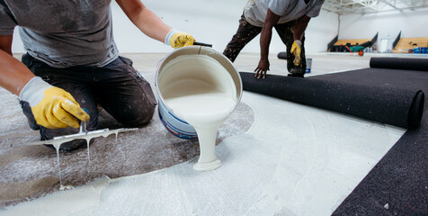Construction workers pouring glue and laying down flooring in warehouse