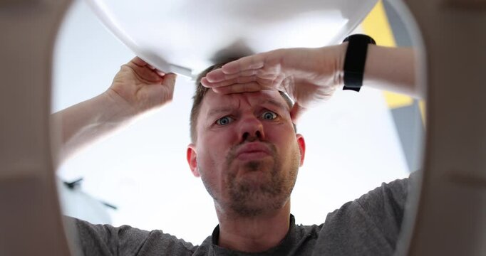 Man opens toilet lid and looks thoughtfully. Sewer blockage and toilet cleaning concept