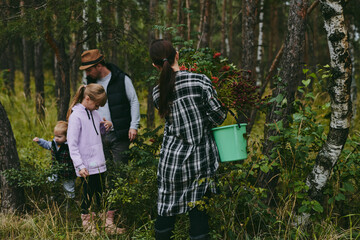 Happy family on a walk in the forest picking berries and herbs, traveling along paths and stones mom dad and children