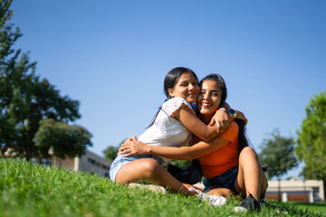 Fototapeta premium Two Latina sisters hugging in a park, one a teenager and one a young adult