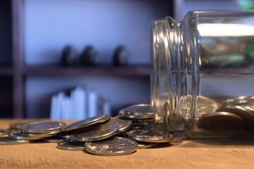 Glass jar of Indonesian Rupiah coins spilled on wooden table in a living room