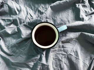 A cup of coffee on a crumpled sheet. Morning coffee on the bed. Crumpled sheet and morning coffee.