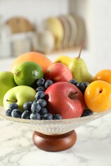 Glass vase with different fresh fruits on white marble table, closeup