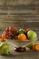 Glass vase with different fresh fruits on wooden table, space for text