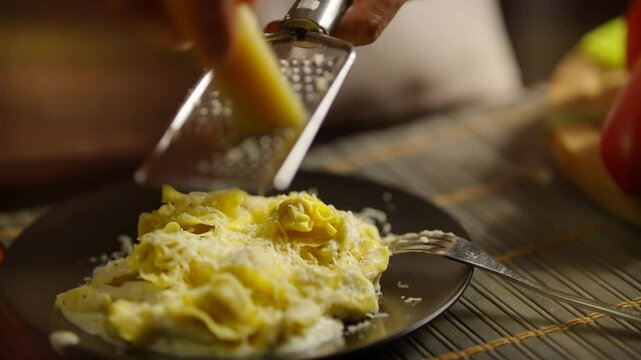 Freshly grated cheese on tortellini served on dark plate	