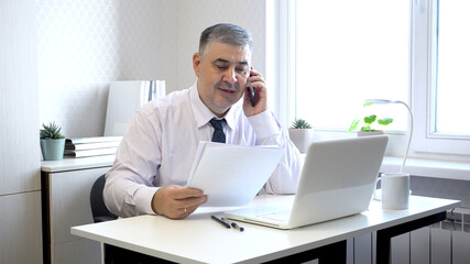 Man Working with Documents and Talking on Phone in Office