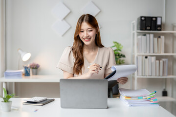 A woman is sitting at a desk with a laptop and a stack of papers