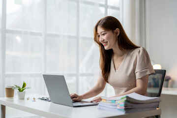 A woman is sitting at a desk with a laptop and a stack of papers