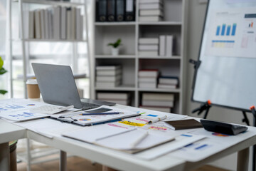 A cluttered desk with a laptop, calculator, and several papers