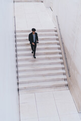 Aerial top of millennial hipster guy with modern digital tablet in hand at urban setting, trendy dressed young man with touch pad in hands going down at city stairs during travel destination