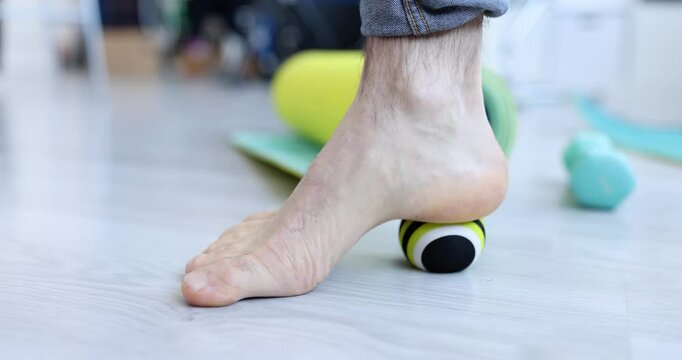 Man makes therapeutic foot massage with ball. Exercises with massage ball concept - Powered by Adobe